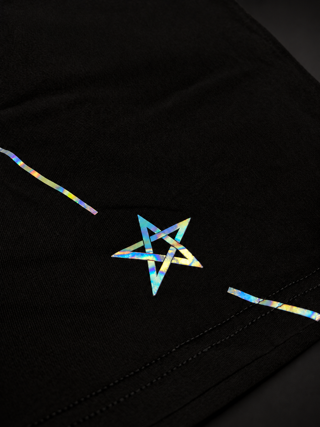 Close-up of the iridescent star and line beside the hem of the ELAISSAOUI WLAD AISSA T-shirt.